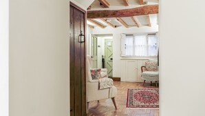 A hallway with a wooden floor, a door, a chair, and a window with curtains. - Honeypot Cottage-Lovely Bolthole in Stow (Cheltenham)