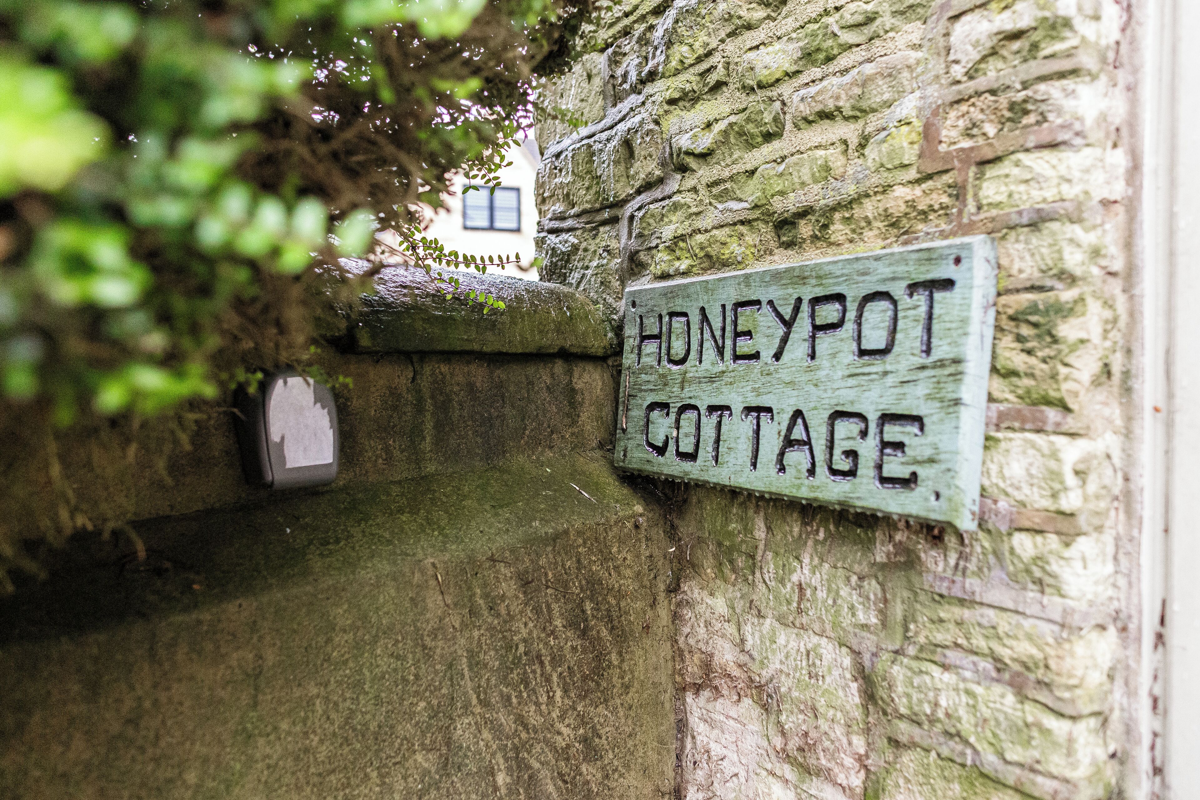 Uma parede de pedra rústica com uma placa de madeira desgastada que diz 'Honeypot Cottage'.