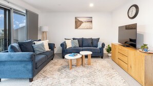 A modern living room with two sofas, a coffee table, a TV, and a large window. - Creek House (Ocean Grove)
