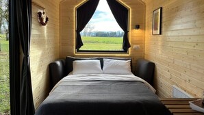 A cozy bedroom with a large bed, a window with curtains, and a view of the outdoors. - Lisi Grun Tiny House by Tiny Away (Sattledt)