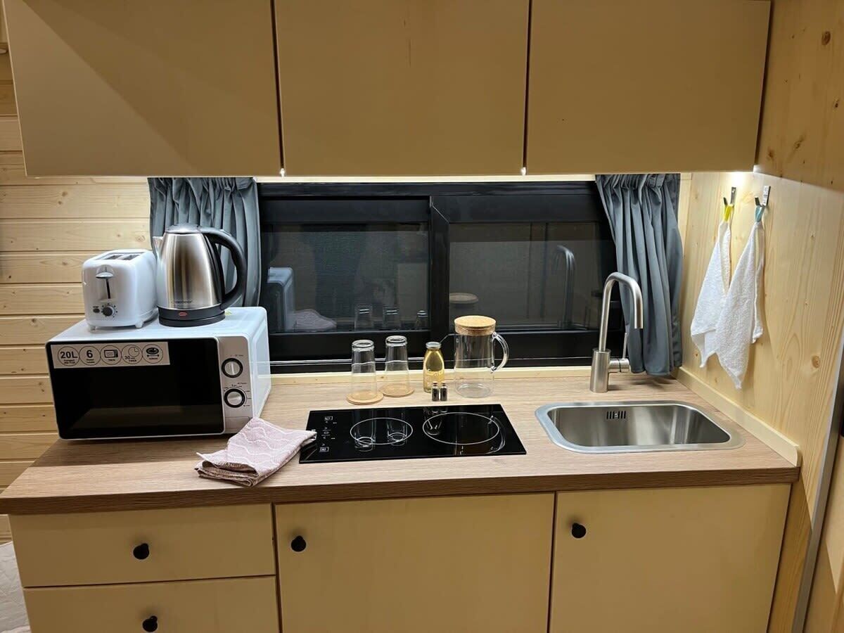 A compact kitchenette with a microwave, toaster, kettle, and a sink.
