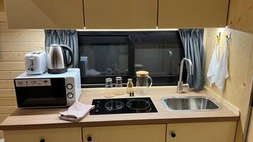 A compact kitchenette with a microwave, toaster, kettle, and a sink.