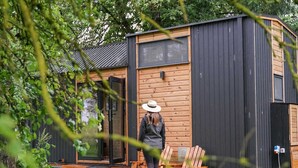 A modern cabin with a wooden exterior and a black roof, featuring a large window and a door. - Lisi Grun Tiny House by Tiny Away (Sattledt)