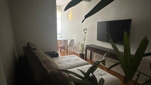 Una sala de estar acogedora con un sofá, una televisión y un rincón de comedor al fondo.