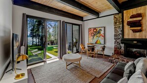 A modern living room with a fireplace, a large window, and a view of a garden. - Kings Beach Escape w/ Patio & Pool Access (Kings Beach)