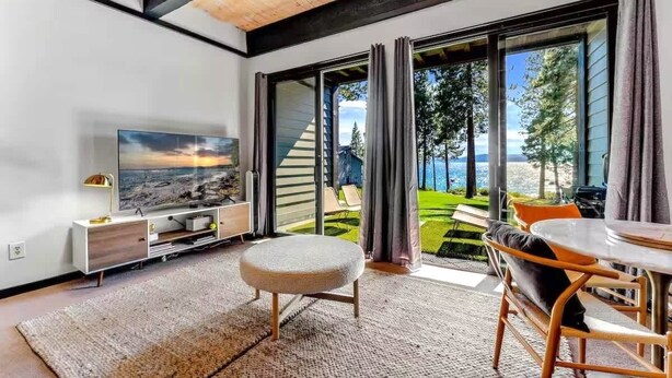 A modern living room with a large TV, a sofa, and a dining area with a table and chairs. - Kings Beach Escape w/ Patio & Pool Access (Kings Beach)