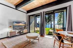 A modern living room with a large TV, a sofa, and a dining area with a table and chairs. - Kings Beach Escape w/ Patio & Pool Access (Kings Beach)