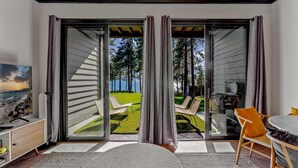 A modern room with a sliding glass door leading to a balcony with a lawn and a view of trees and water. - Kings Beach Escape w/ Patio & Pool Access (Kings Beach)