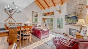 Ein geräumiges Wohnzimmer mit Holzboden, einem Essbereich mit Holztisch und -stühlen, einem roten Ledersofa und einem Kamin.