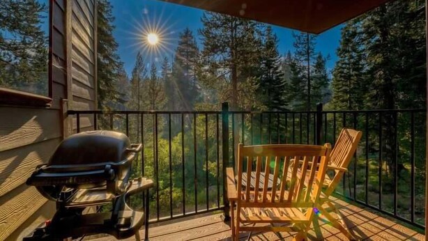 Eine Holzterrasse mit Grill und Stuhl, mit Blick auf ein bewaldetes Gebiet.