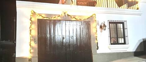 A building with a dark wooden gate, a white facade, and a balcony with string lights.