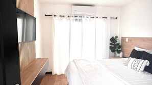 Un dormitorio con cama, televisor, planta y pared de paneles de madera.