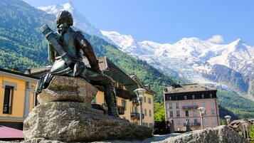 A statue of a person with a telescope, set against a backdrop of snow-capped mountains and buildings.