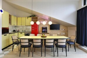 Un comedor con una mesa larga y sillas, una cocina con armarios amarillos, un refrigerador rojo y un televisor de pantalla plana en la pared.
