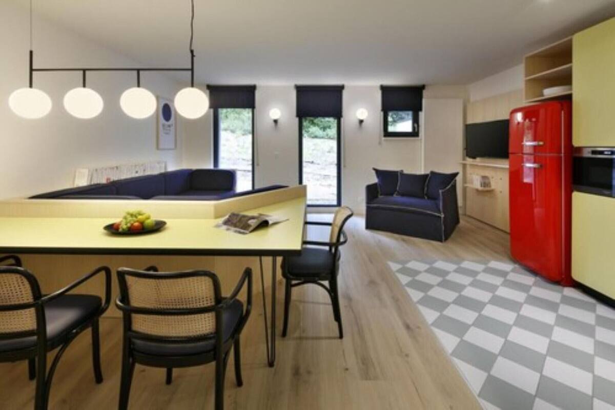 A modern kitchen with a central island, a dining area with chairs, a sofa, and a red refrigerator.