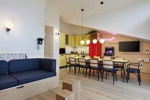 A modern living room with a sofa, dining area with chairs, a kitchen with yellow cabinets, and a TV mounted on the wall.