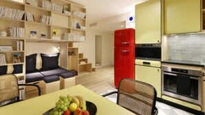 Un espacio habitable compacto con sofá, mesa de comedor y cocina equipada con refrigerador y horno.