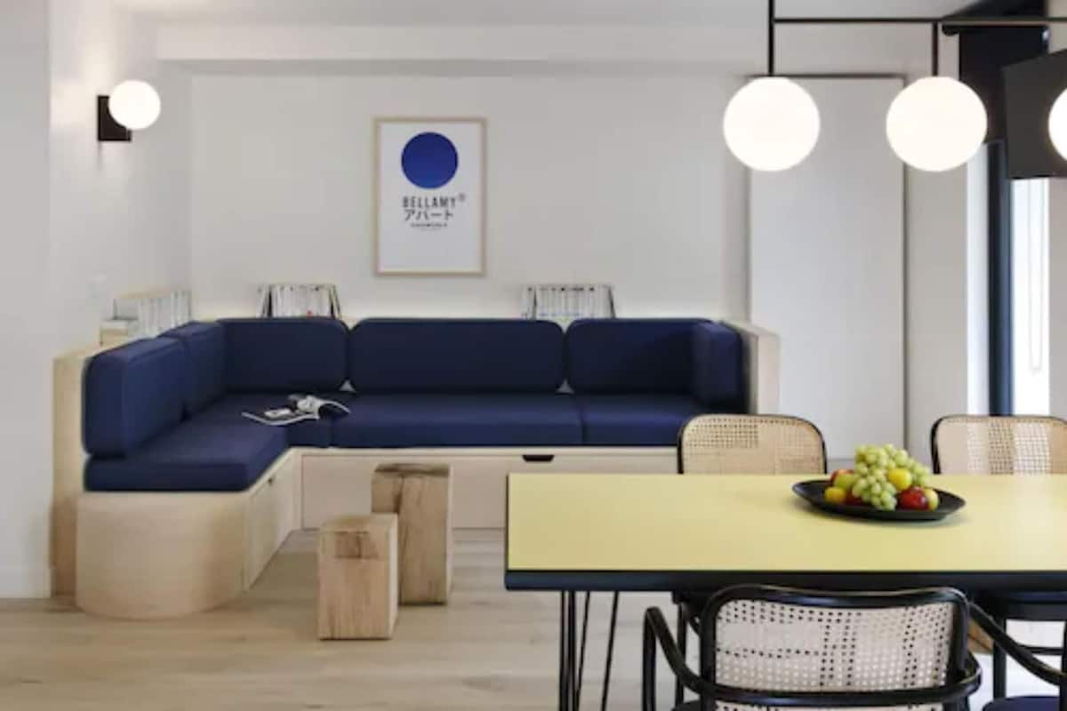 A modern living room with a blue sofa, a yellow dining table, and a fruit bowl.