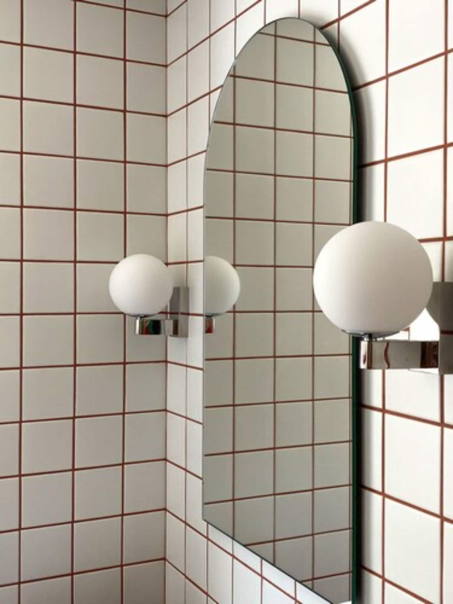 A bathroom with tiled walls, a mirror, and two wall-mounted light fixtures.