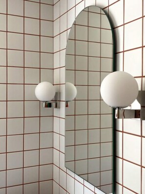 Un baño con paredes de azulejos, un espejo y dos lámparas fijadas a la pared.