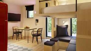 Una habitación compacta con una cama litera, una mesa de comedor con sillas y un pequeño rincón de descanso con cojines.