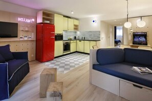 A modern living room with a sofa, a red refrigerator, and a kitchen area with yellow cabinets. - Appartements Bellamy (Chamonix-Mont-Blanc)