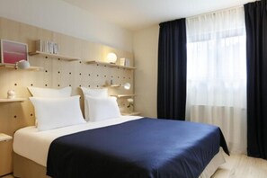 A hotel room with a bed, bedside tables, a wall-mounted shelf with books, and a window with curtains. - Appartements Bellamy (Chamonix-Mont-Blanc)