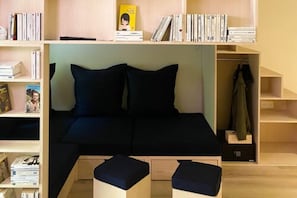 A bedroom with a bed, two pillows, a nightstand, a bookshelf, and a coat rack.