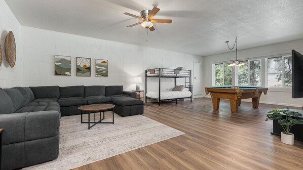 A modern living room with a sectional sofa, a pool table, a bunk bed, and artwork on the walls.