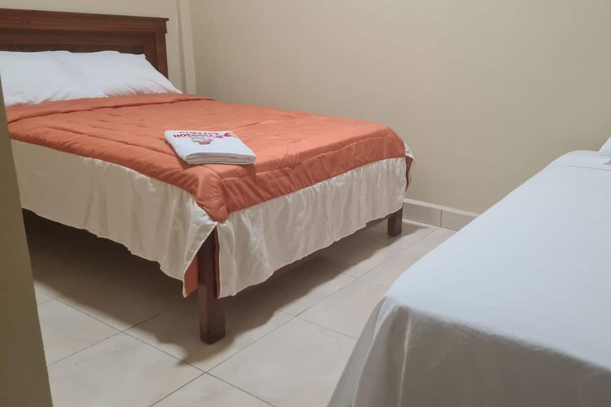Una habitación de hotel con dos camas, una con colcha naranja y la otra con sábana blanca.