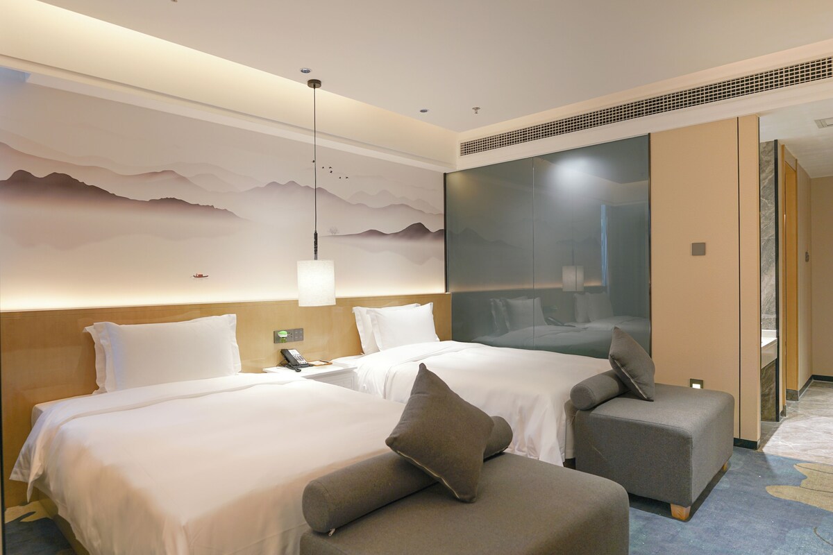 Ein Hotelzimmer mit zwei Betten, einem Sofa, einem Telefon und einer Wand mit Bergmotiv.
