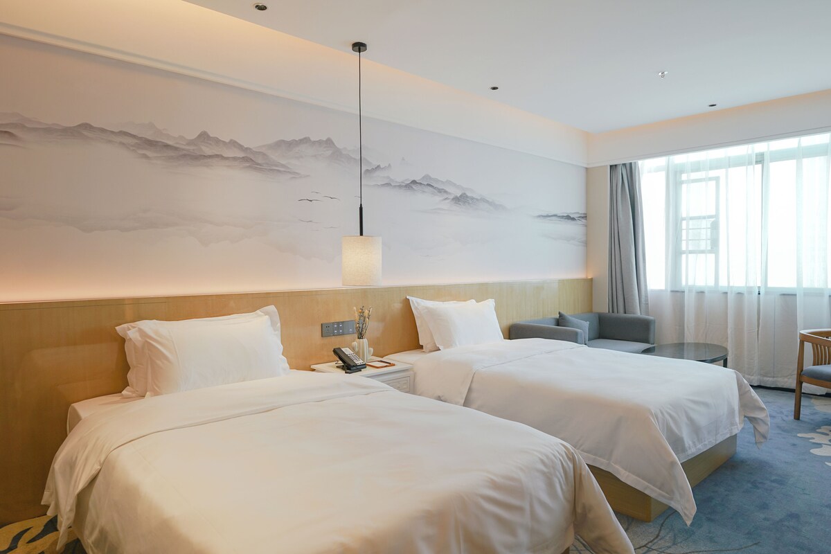 Ein Hotelzimmer mit zwei Betten, einem großen Wandbild, einem Schreibtisch mit Lampe und Blick ins Freie.