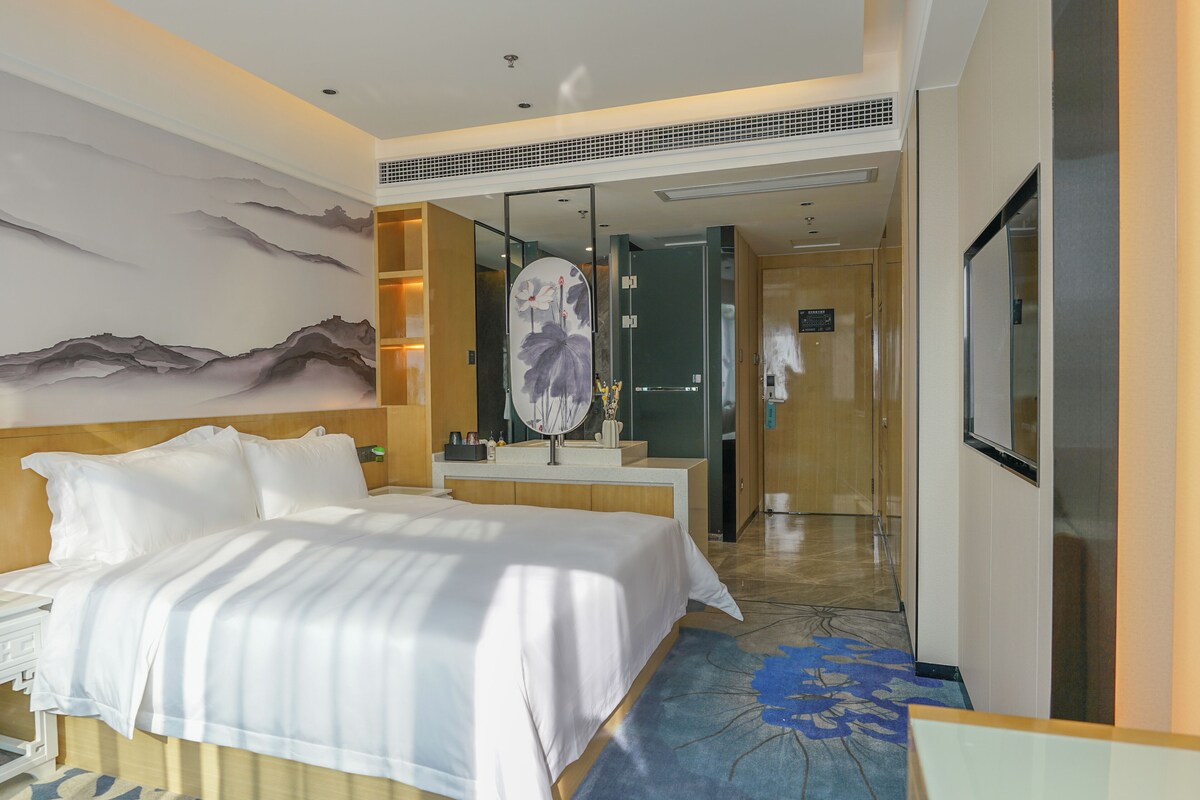 Ein Hotelzimmer mit einem großen Bett, einem Badezimmer mit Spiegel und Blick auf den Flur.
