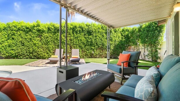 Un patio couvert aménagé avec du mobilier d’extérieur, un foyer et une vue sur une haie bien entretenue.