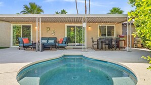 Un espace piscine extérieur moderne doté d’un patio couvert, de coins salon et d’un barbecue.