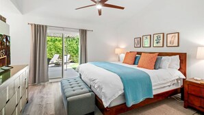 Une chambre avec un grand lit, un ventilateur de plafond, un bureau et une vue sur l’extérieur.