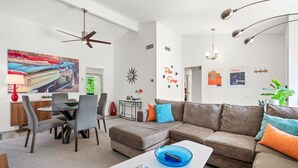 Un salon moderne avec un canapé d’angle, un coin repas doté d’une table ronde et un ventilateur de plafond.