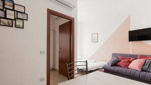 A room with a dining table, a sofa, a TV mounted on the wall, and a door leading to another room. - GuestHost - Affori FN Modern Apartment x4! (Milano)