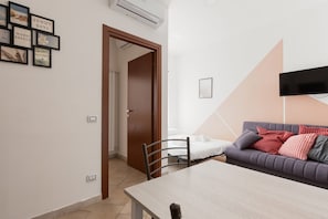 Une pièce comprenant une table à manger, un canapé, un téléviseur fixé au mur et une porte donnant sur une autre pièce.