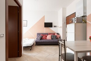 Un espacio habitable compacto con sofá, mesa de comedor, televisor montado en la pared y una pequeña cocina.