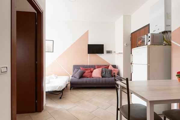 Un espacio habitable compacto con sofá, mesa de comedor, televisor montado en la pared y una pequeña cocina.