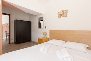 Una habitación de hotel con cama, armario, mesita de noche con lámpara y espejo en la pared.