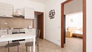 A modern kitchen with a dining area, a bed in the adjacent room, and a hallway with a door. - GuestHost - Affori FN Modern Apartment x4! (Milano)