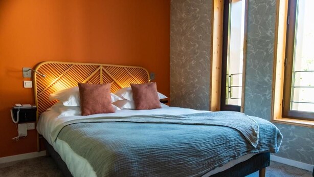 A bed with a geometric headboard, two pillows, and a blue blanket. - Logis Hotel Le Chalet Altitude (Pierre-Percée)