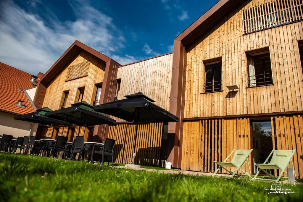 A modern building with wooden exterior walls, outdoor seating with umbrellas, and a clear sky.