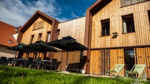 A modern building with wooden exterior walls, outdoor seating with umbrellas, and a clear sky. - Logis Hotel Le Chalet Altitude (Pierre-Percée)
