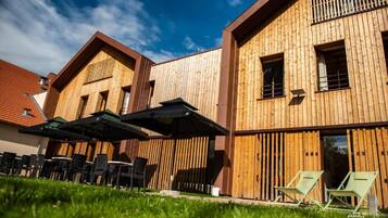 A modern building with wooden exterior walls, outdoor seating with umbrellas, and a clear sky.