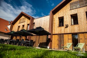 Un bâtiment moderne aux murs extérieurs en bois, doté d’une terrasse avec des parasols, et surplombant un ciel dégagé.