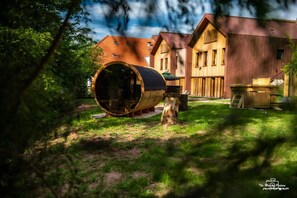 A rustic wooden cabin with a large barrel in the foreground, surrounded by lush greenery. - Logis Hotel Le Chalet Altitude (Pierre-Percée)