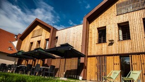 A modern building with wooden exterior walls, outdoor seating with umbrellas, and a clear sky. - Logis Hotel Le Chalet Altitude (Pierre-Percée)